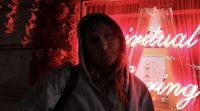 a girl wearing a hoodie in front of a red neon sign